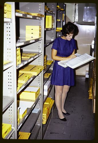 Woman standing next to some shelving, looking at a book.