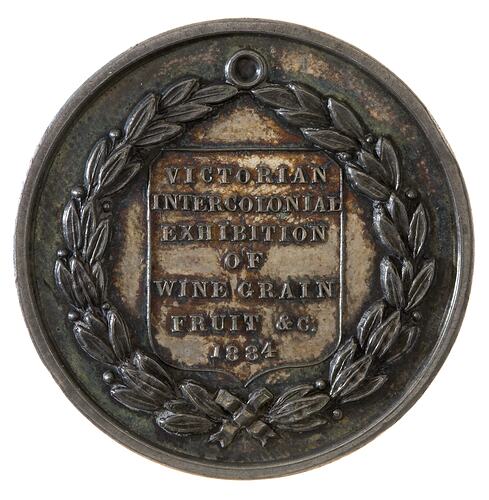 Round silver medal with thick olive wreath framing shield with raised text.