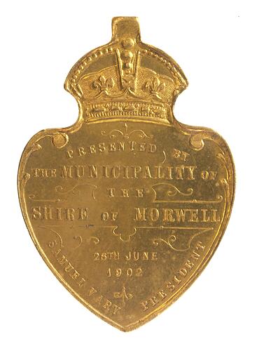 Shield shaped medal with crown at top and text below.