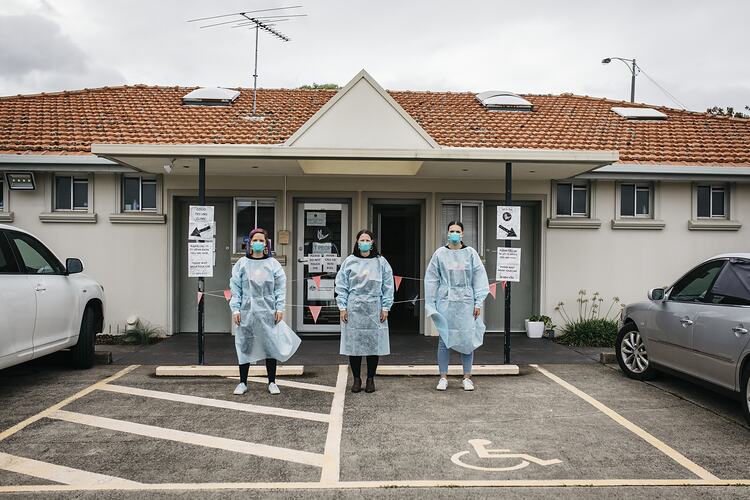 Staff Members Dressed in Gowns and Masks Stand in Carpark at First Peoples Health and Wellbeing Clinic, Thomastown, Wurundjeri Woi Wurrung Country, Victoria, 21 Mar 2021