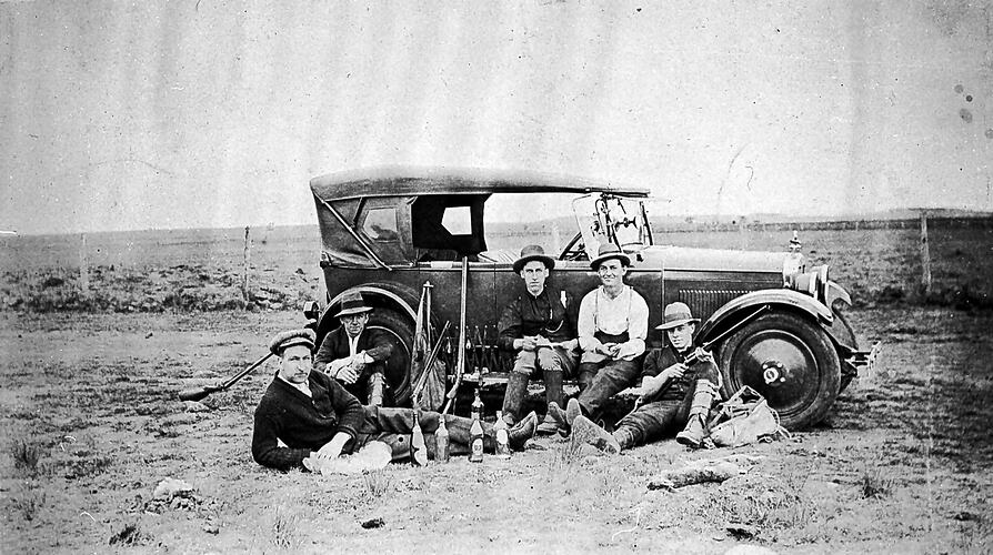 [Shooters drinking beer beside their car, 1920s]