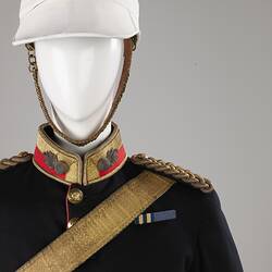 Detail of navy officer's jacket with gold sash, epaulettes. Brass buttons. Red and gold collar, white helmet.