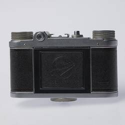 Back of black and silver camera. Top hinged panel in centre. Two dials on top.