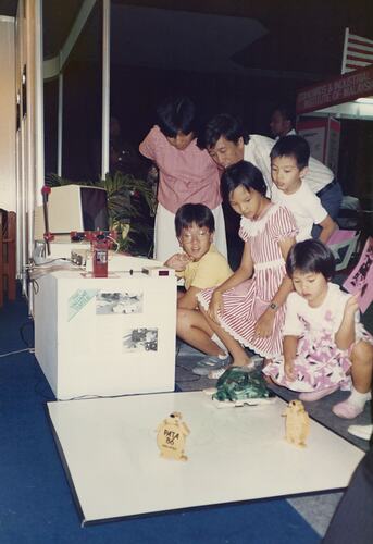 Adults and a child watching a turtle robot on a table.