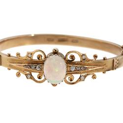Gold bracelet with central oval white opal, supported by rose cut diamonds and delicate gold filigree-style detail.