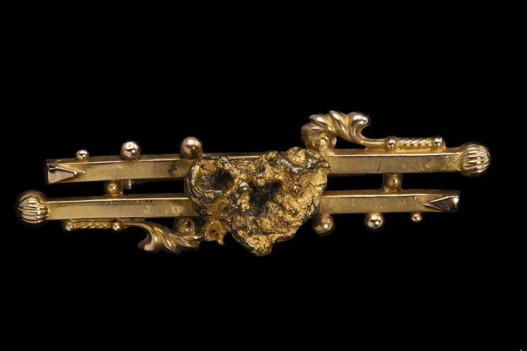 Gold double bar brooch with decorative detailing. Features small natural nugget in centre.