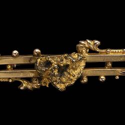 Gold double bar brooch with decorative detailing. Features small natural nugget in centre.