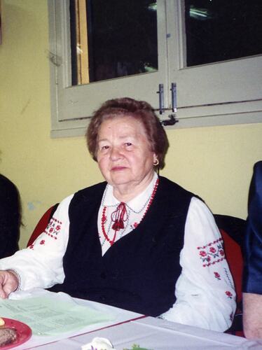 Woman posing, seated at table wearing Ukrainian national dress.