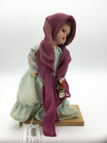 A doll dressed in a pale green dress and purple scarf