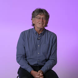 Seated man in blue shirt with purple background.