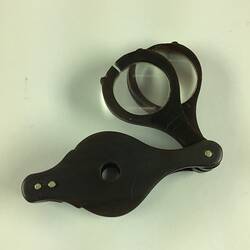 Black loupe with two round hinged magnifying glasses that slide into the case.