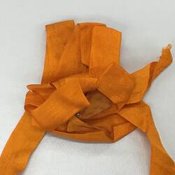 Detail of rosette made from folded and looped bright orange ribbon. Pinned through centre, with a red white and blue ribbon.