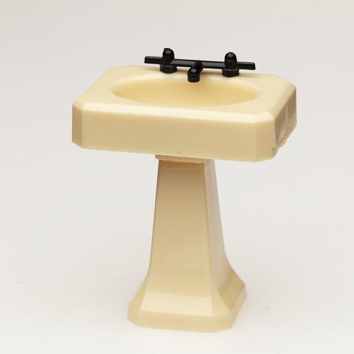Toy bathroom sink made of cream coloured moulded plastic. Two faucets.