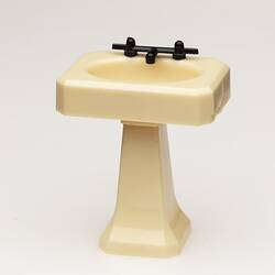 Toy bathroom sink made of cream coloured moulded plastic. Two faucets.