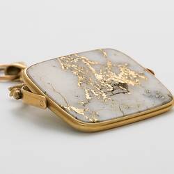 Rectangular pendant featuring white gold-bearing quartz in a gold setting, complimented by a delicate branch-like motif at the top.