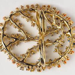 Underside view of large-scale, two-fingered, open work gold ring set with multicoloured microplastics.