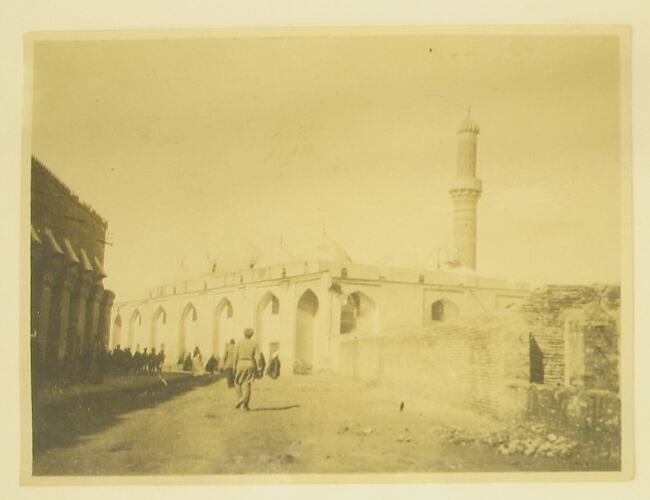 People on street flanked by buildings and minaret.