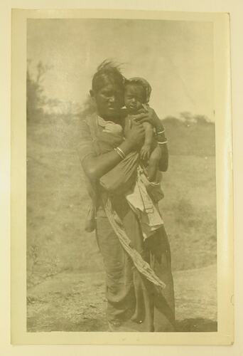 Indian woman standing outdoors holding a child.