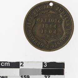 Round bronze coloured medal with inscribed shield and text surrounding.