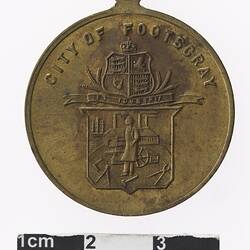 Round medal with coat of arms above a many standing in front of a factory, text above.