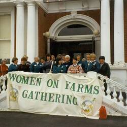 Women standing on front steps of building with banner.