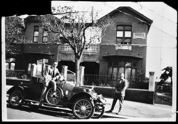 Two men, automobile in front of house.