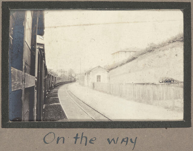 View of a train station from window of a train, with sloping landscape behind.