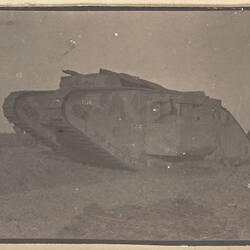 Tank in field, with two soldiers partly visible behind left side of tank.