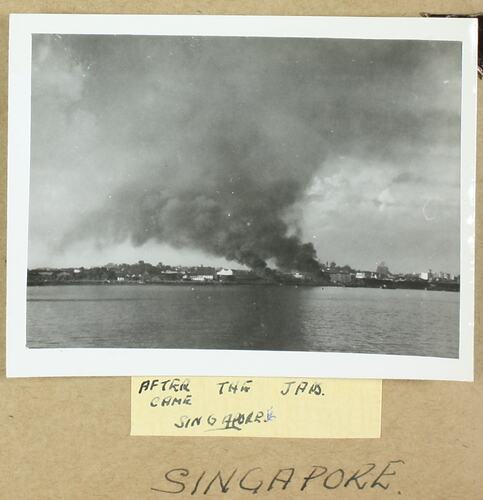 Harbour with land, buildings and billowing smoke in the background.