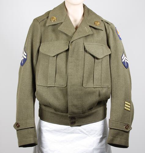 Khaki wool cloth jacket, two breast pockets, belt buckle waist. Brass collar badges, cloth badges on sleeves.