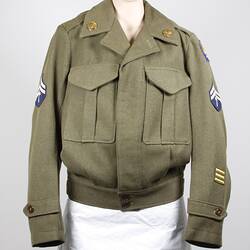 Khaki wool cloth jacket, two breast pockets, belt buckle waist. Brass collar badges, cloth badges on sleeves.