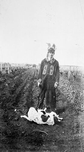 Man wearing an Indian costume. He is in a vineyard and has two dogs at his feet.