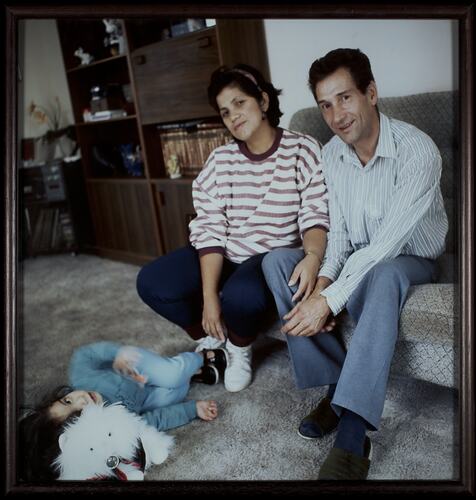Woman and man sitting on couch. Young child with toy lays on floor in front of them.