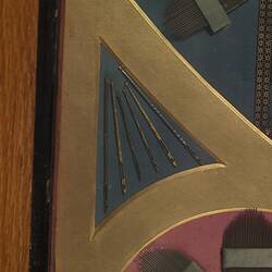 Detail of panel made of needles, crochet hooks, surgical needles, and other needles and needle cases. In red, black and yellow.