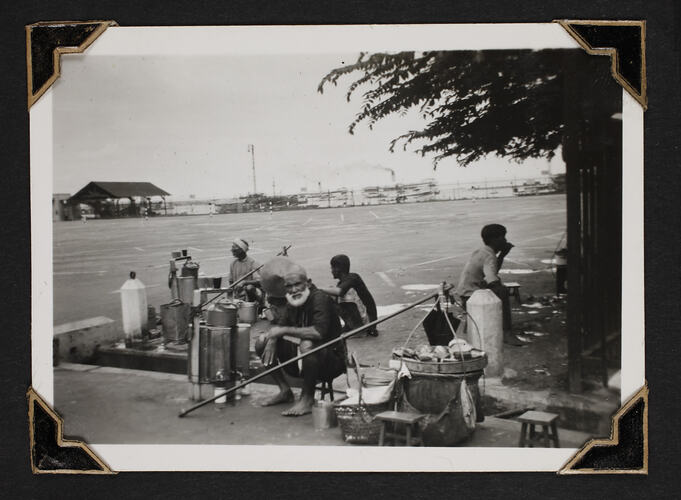Men sitting on ground with food cooking equipment.