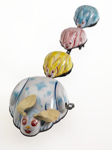 Wind-up metal white and blue rabbit towing three smaller yellow, pink then blue rabbits.