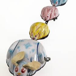 Wind-up metal white and blue rabbit towing three smaller yellow, pink then blue rabbits.