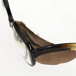 Side view of plastic prosthetic glass left eye with upper left cheek, eyebrow and eyelashes attached to brown plastic spectacles.