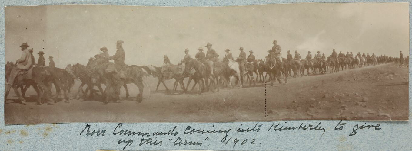 Line of servicemen on horseback walking down dirt road.