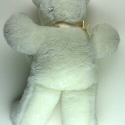 Wool plush white teddy bear with satin ribbon on its neck.