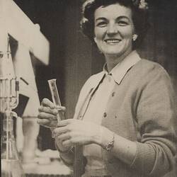 Woman in cardigan holding test tube.