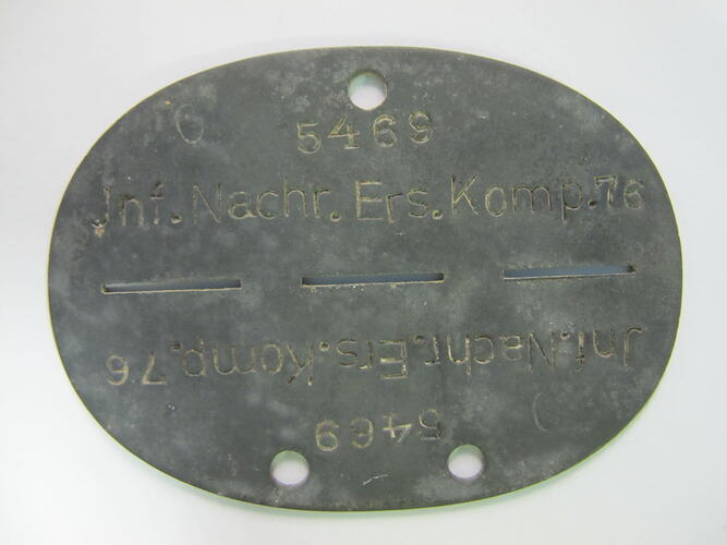 Oval shaped metal disc with dividing line down centre and inscribed text.