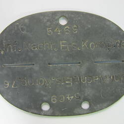 Oval shaped metal disc with dividing line down centre and inscribed text.