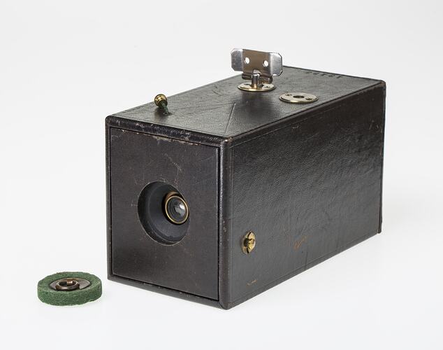 Dark leatherette-covered rectagular card box. Round hole at end has lens, drawstring shutter string on top.