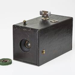 Dark leatherette-covered rectagular card box. Round hole at end has lens, drawstring shutter string on top.