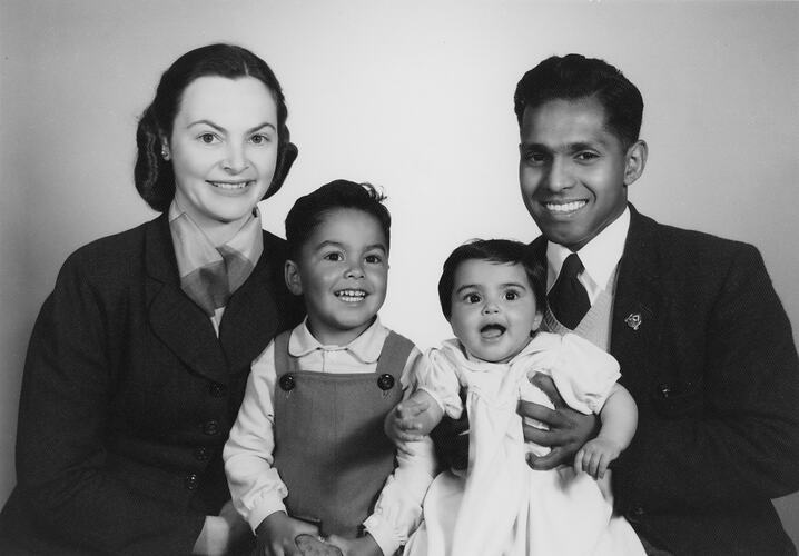 Smiling man and woman seated, posing with two young children.