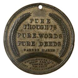 Round medal with hole at top and fern leaves framing central text.