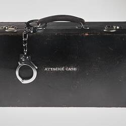 Black leather briefcase marked 'Attache Case' with handcuffs on the handle.