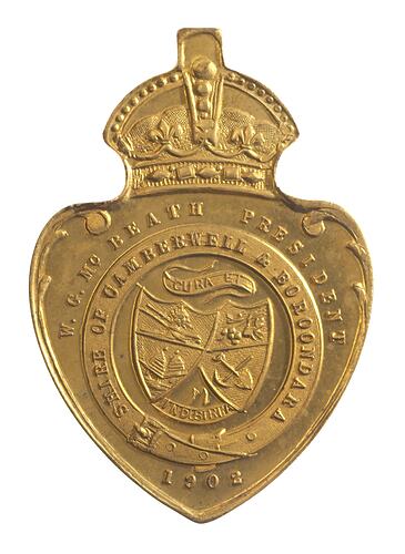 Shield shaped medal with crown and loop at top. Has two crossed shields featuring plough, sheaf, beehives.