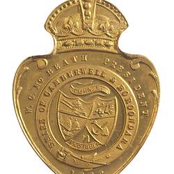 Shield shaped medal with crown and loop at top. Has two crossed shields featuring plough, sheaf, beehives.